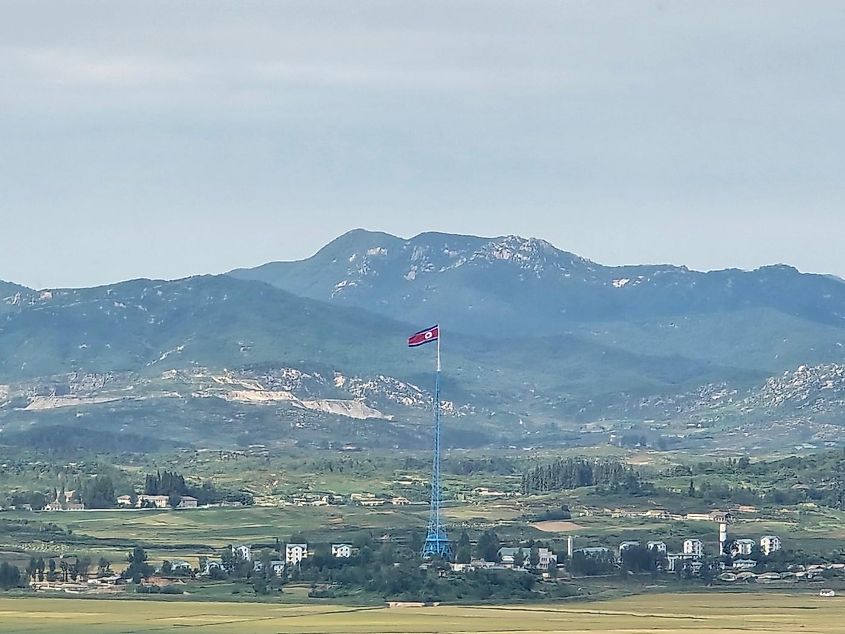 A tall North Korean flagpole stands amongst a green, mountainous landscape.