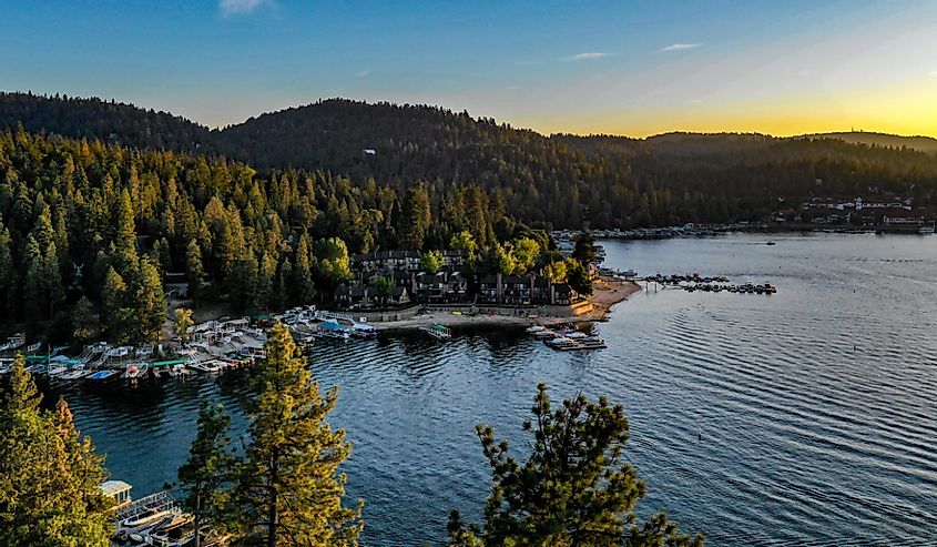 Aerial view of Lake Arrowhead at dusk with green trees, blue water and sky, yellow, gold, orange sunset in the San Bernardino Mountains, California