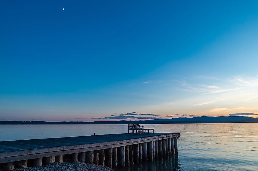 Sliver moon at dusk with a view of a wooden dock at the shoreline of Flathead Lake, near Polson, Montana