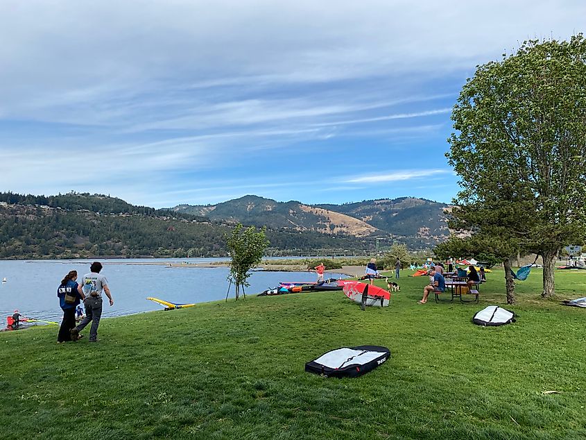 Windsurfers chilling on a grassy riverside park, waiting to launch.