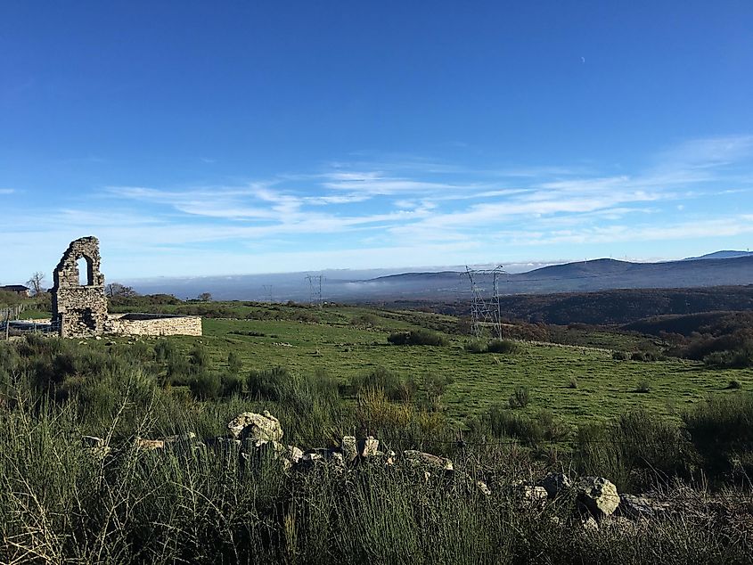 A partial stone ruin sticks up from the grassy slopes overlooking a green, mountainous landscape. 