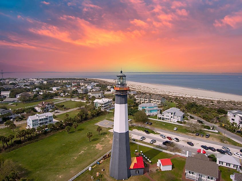 Aerial shot of Tybee Island Beach, featuring the lighthouse, blue ocean water, sandy beach, homes, and lush green trees and grass in Tybee Island, Georgia, USA.