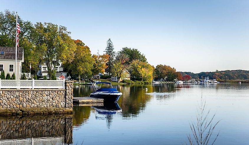 Waterside houses among trees with boats moored to wooden jetties on a clear autumn day along the Connecticut River, Essex