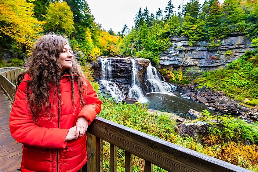 Young woman standing on the wooden boardwalk deck overlooking Blackwater Falls State Park in West Virginia during the autumn fall season