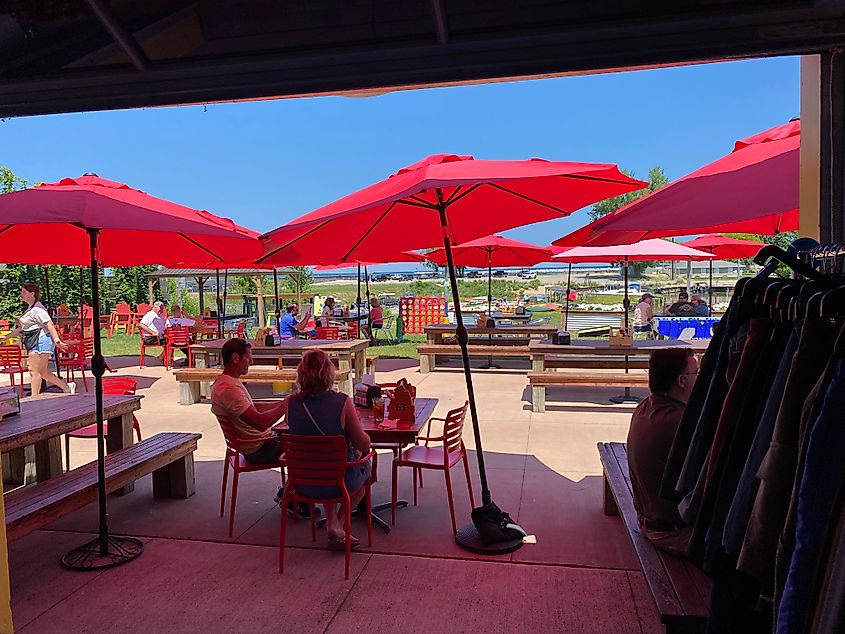 Looking through a door to an open-air patio filled with red umbrellas and casual clientele.