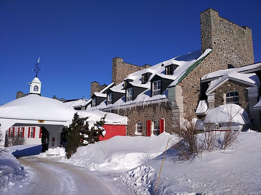 Editorial Photo Credit: Ann Dr via Shutterstock. Baie-Comeau, Quebec / Canada - January 27 2018: view of Hotel le Manoir covered in snow in the morning of a sunny winter day. Leafless trees, blue sky, white snow, grey building.