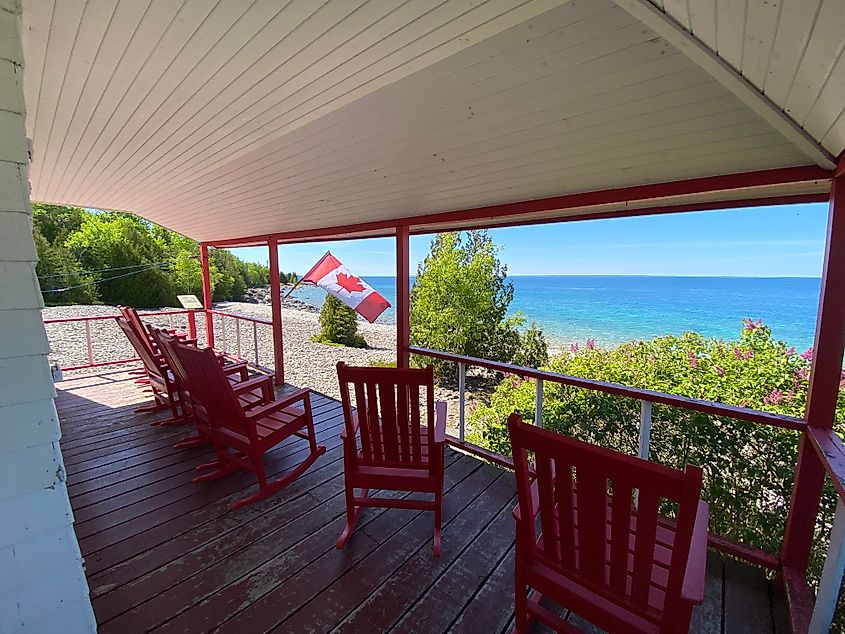A red and white house porch with a Canadian flag, overlooking a beautiful shoreline