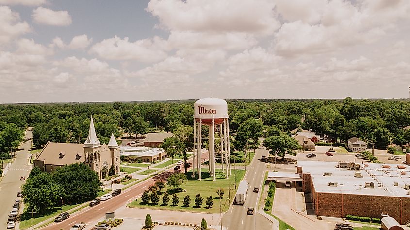 An aerial view of downtown Minden, Louisiana, showcasing the iconic water tower, a historic church with twin spires, and surrounding streets and buildings