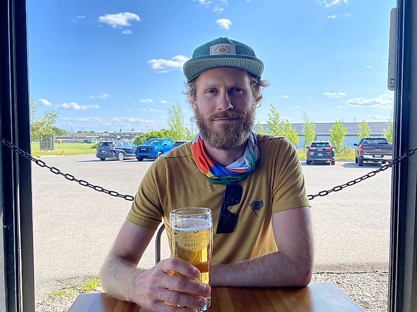 A man sits at an open-air table with a craft pint and a smile 