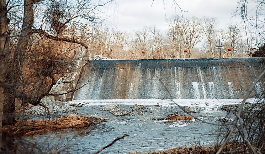 A beautiful view of a waterfall and leafless tress against cloudy sky during daytime at Marshall Riverwalk, Marshall, Michigan