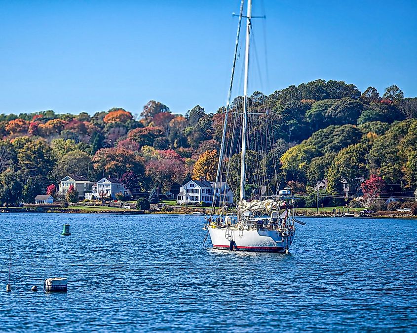 Sailboat anchored on the Mystic River in Mystic, Connecticut, with autumn foliage along the shoreline