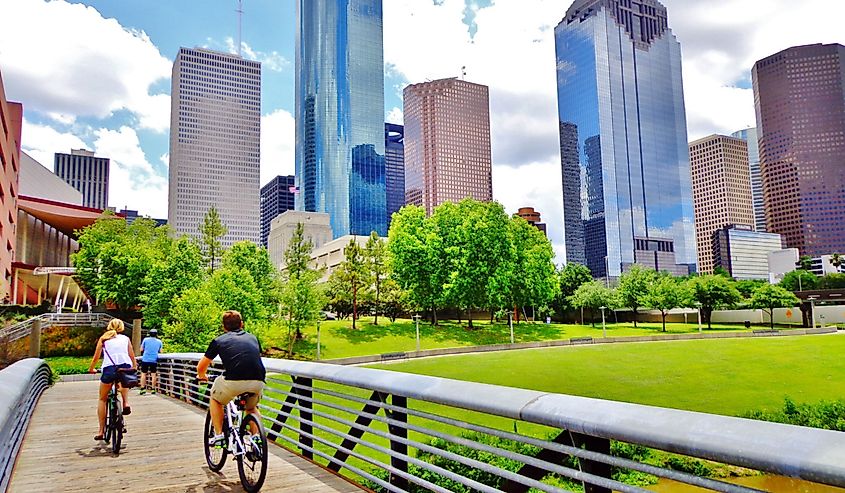 Bicyclists cross wooden bridge in Buffalo Bayou Park, with a beautiful view of downtown Houston (skyline / skyscrapers) in background on a summer day - Houston, Texas, USA
