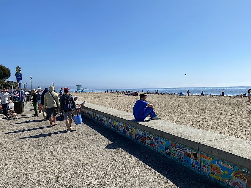 A small crowd walks along a beachside walkway on a bluebird day.