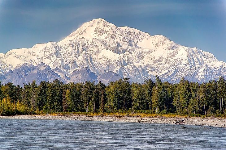 Denali rising far above the surrounding Alaskan lowlands and a river in the foreground.
