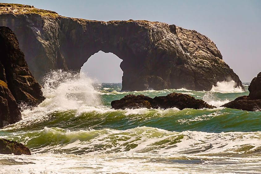 Wave crashing against sea stack by Arched Rock on a sunny afternoon in Bodega Bay, Sonoma Coast State Park, California, USA, for themes of turbulence, impact, erosion. Via Shutterstock / Ken Schulze