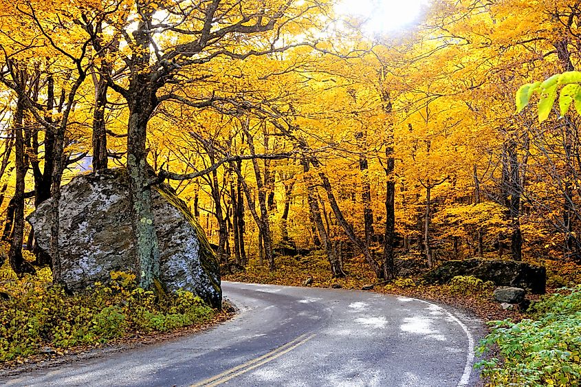 Vibrant autumn colors in the sun with winding Smuggler's Notch road, Vermont, USA.