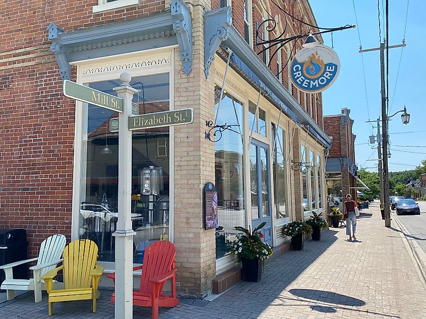 A woman walks past colorful cottage chairs and a brick building housing Creemore Springs Brewery
