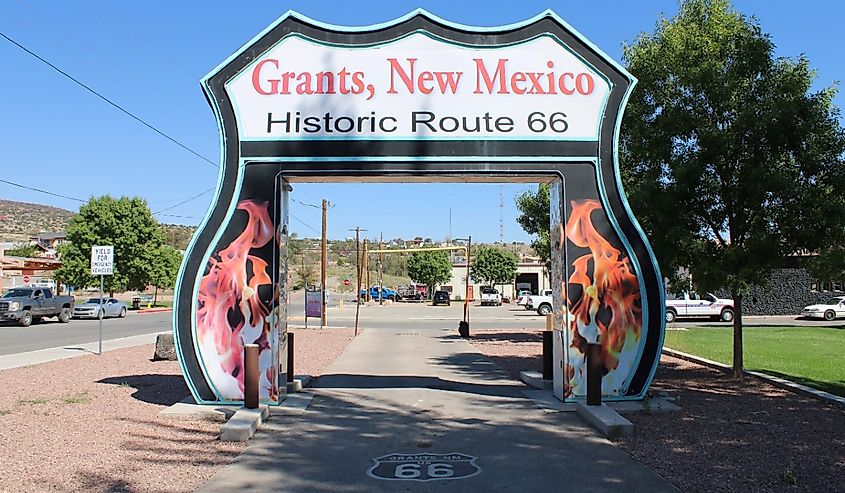 A large sign reads "Grants, New Mexico, Historic Route 66" over a road. Flames decorate the sides, and a Route 66 emblem is painted on the pavement.