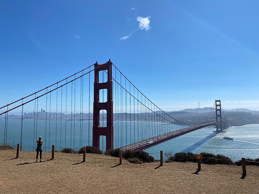 A woman stands atop a Golden Gate Bridge overlook, looking across the strait and back toward San Francisco's skyline.
