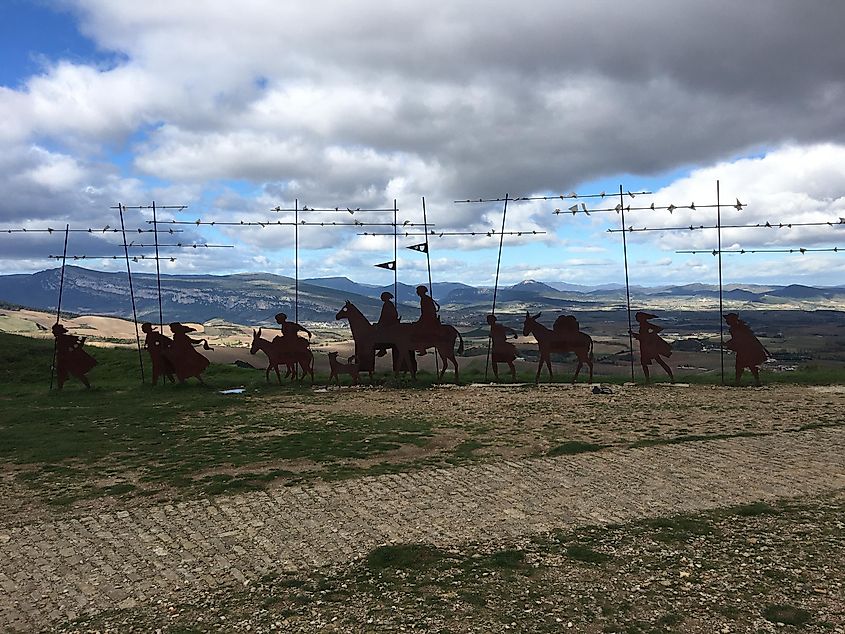 A collection of pilgrim statues at the top of a mountain pass. More mountains can be seen in the background. 