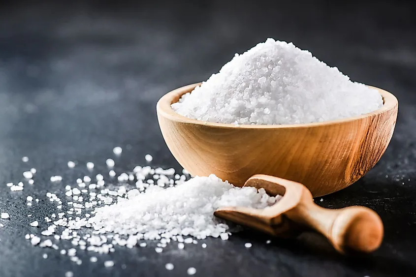 Salt in a wooden bowl and scoop on a dark stone table. 