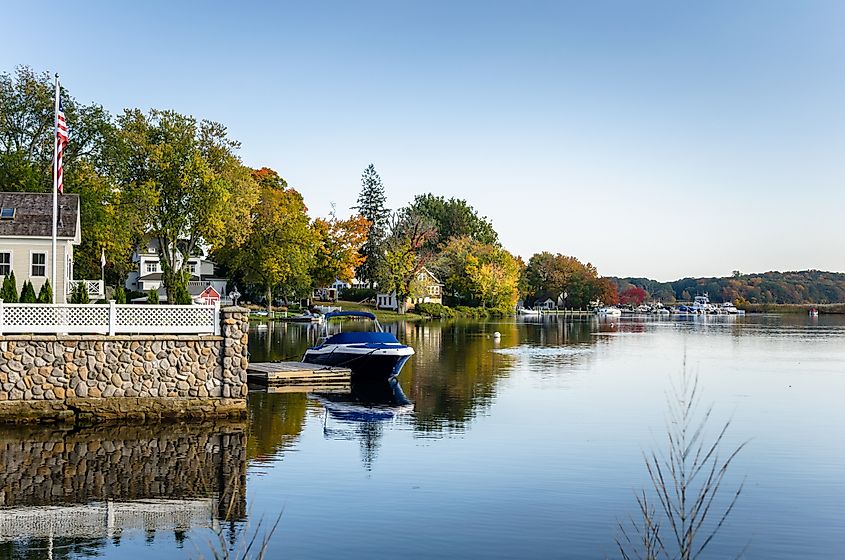 Essex, Connecticut: Waterside houses among trees with boats moored to wooden jetties on a clear autumn day, Connecticut River.