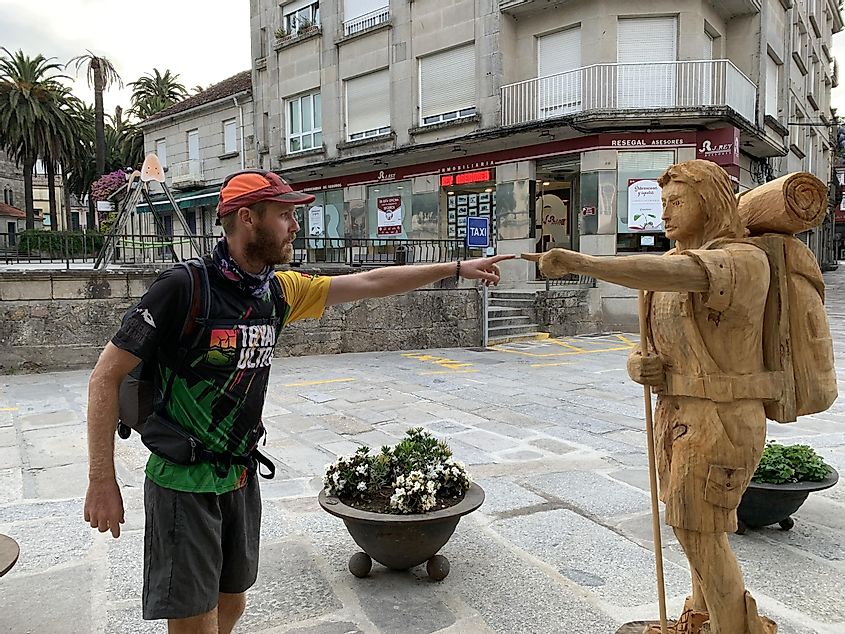 A human pilgrim and a wooden statue of a pilgrim pointing at each other along the Coastal Way. 