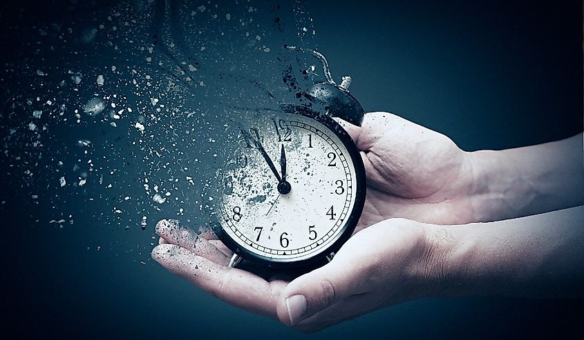 Concept of time passing away, the clock breaks down into pieces. Hand holding analog clock with dispersion effect