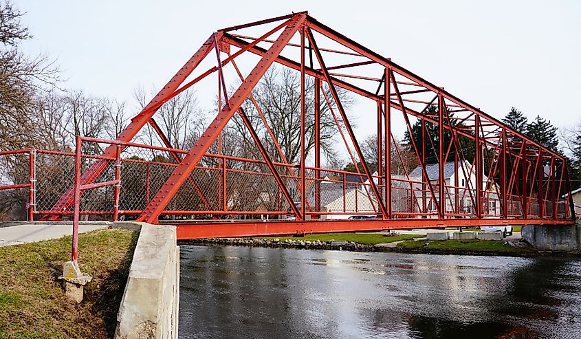 Red gated walking path bridge extends over Rock River that flows through in Mayville, Wisconsin.