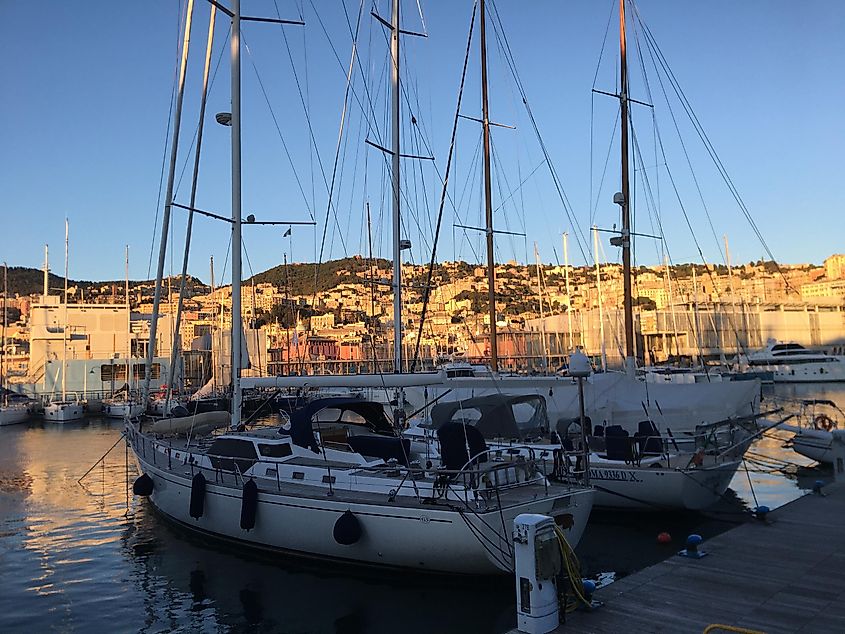 Two sail boats backdropped by the pastel buildings of Genoa, Italy. The sun prepares to set. 