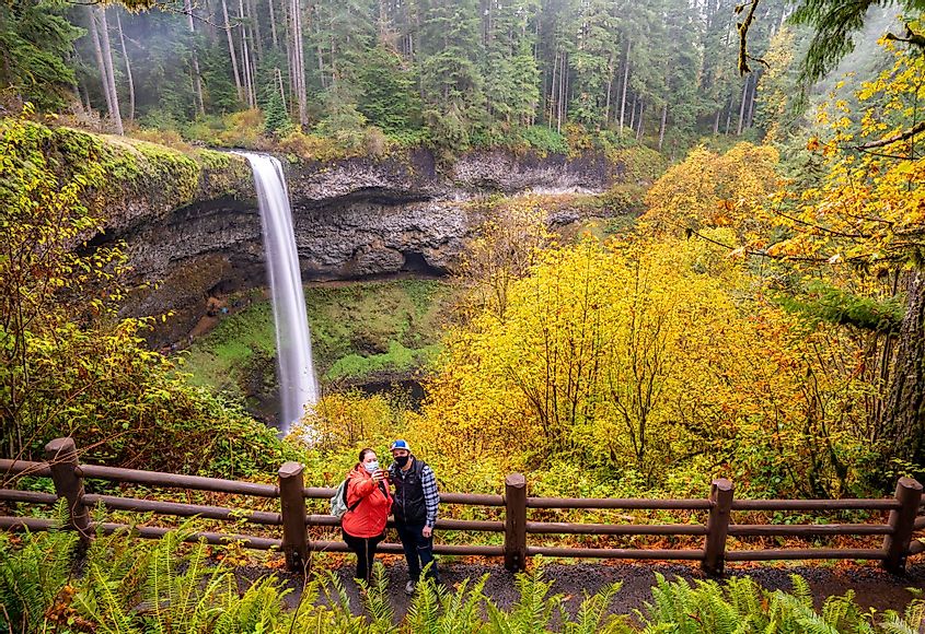 Two people taking selfie photos in front of South Falls at Silver Falls State Park near Silverton, Oregon