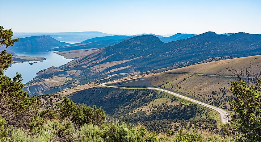 An overlook from the Flaming Gorge Green River Scenic Byway in Utah showing red-colored mountains and high desert plant life, with the twisting highway in the foreground