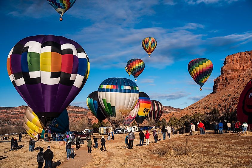 Spectators gather in open fields beneath beautiful red rock mesas to watch hot air balloons during the 'Balloons and Tunes' Festival held in Kanab, Utah, USA, each February.