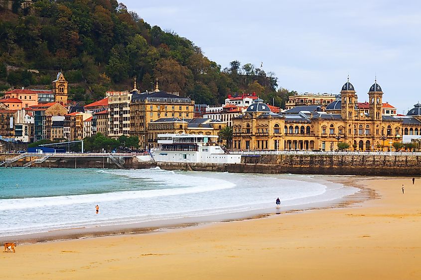 A smooth sandy beach lies before a collection of Spanish buildings on an overcast Fall day