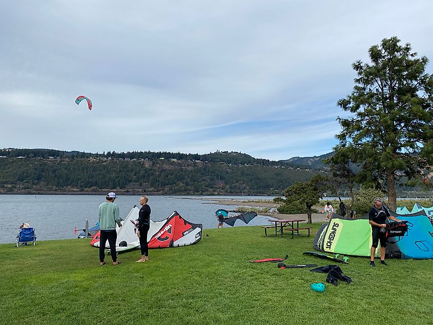 Windsurfers gather on a grassy shore beside the Columbia River. 