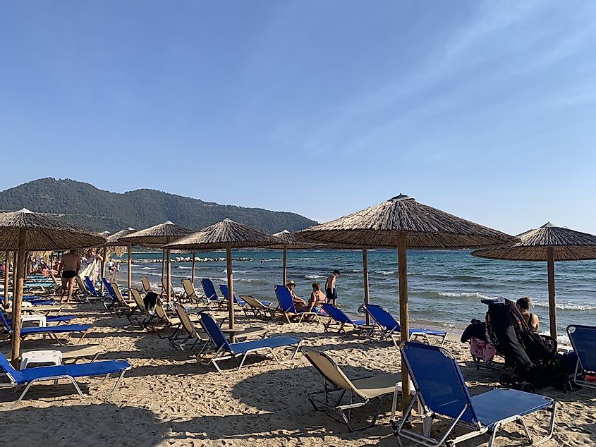 Beach umbrellas and lounging chairs line a sandy beach on the sparkling blue Thracian Sea. 