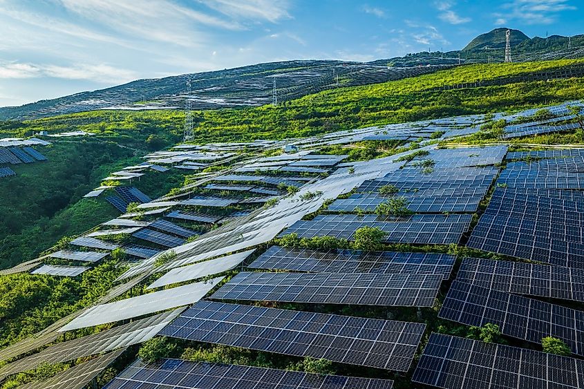 Aerial view of a large-scale solar farm with photovoltaic panels on green mountain slopes in Guizhou, China.