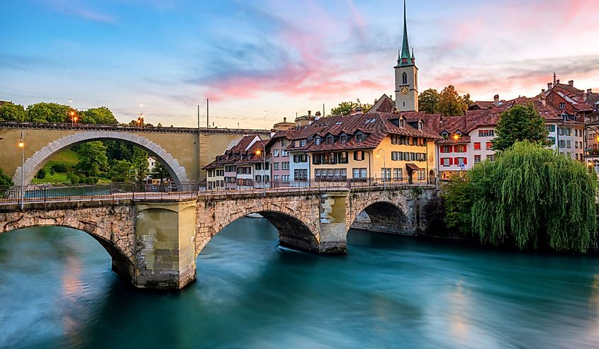 Historical Old Town of Bern city, tiled roofs, bridges over Aare river and church tower on dramatic sunset, Switzerland