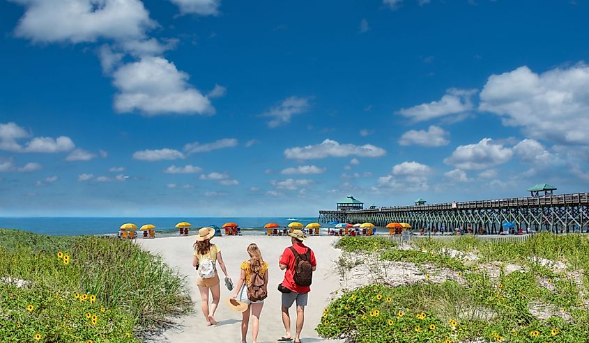 Family walking on the beach. Cloudy sky and pier in the background. Folly Beach, South Carolina USA.