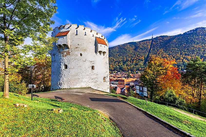 A small green mountain backdrops a red-roofed Romanian Old Town, with a large white tower dominating the foreground.