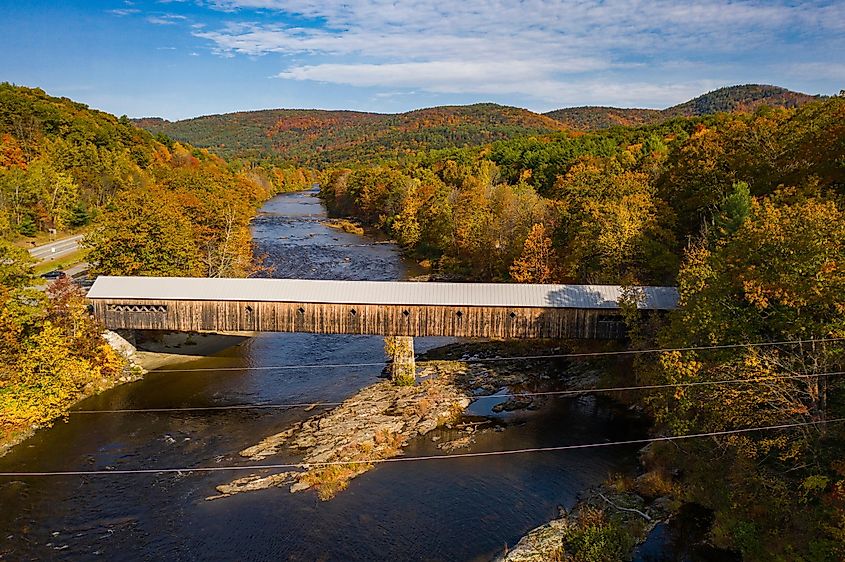 Covered bridge with fall foliage landscape over river in Dummerston, Vermont New England town during autumn season.