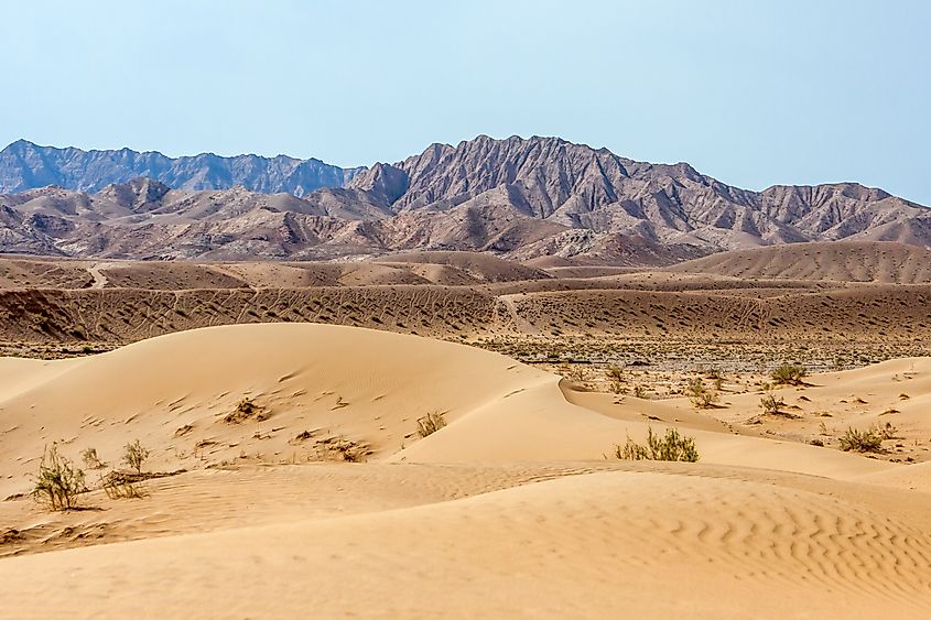 Sand dunes in the Dasht-e Kavir desert, Iran, with mountains in the background under a clear sky.