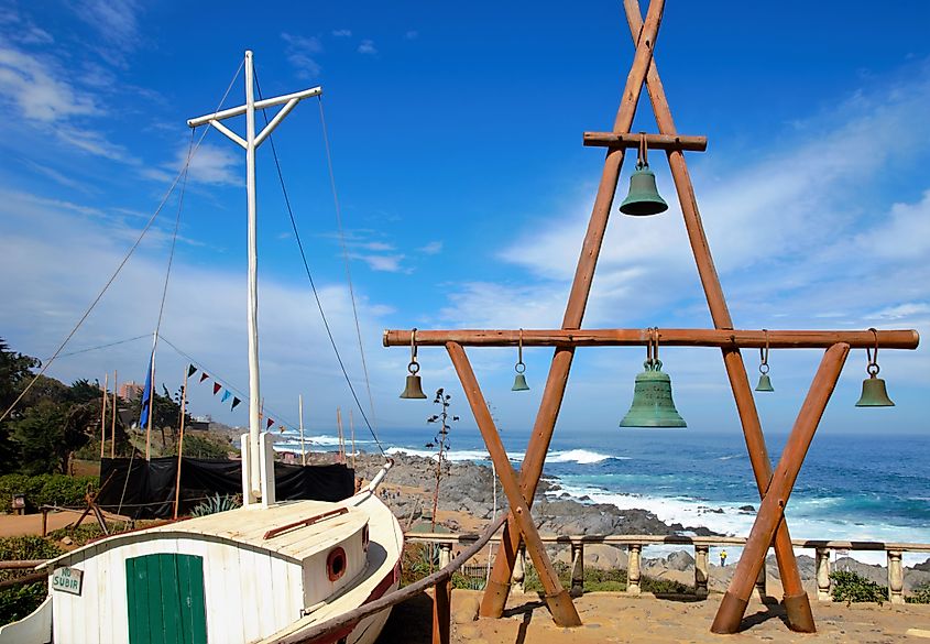 View of the ocean outside Pablo Neruda's house, featuring a wooden construction with green bells and a white boat in the foreground.