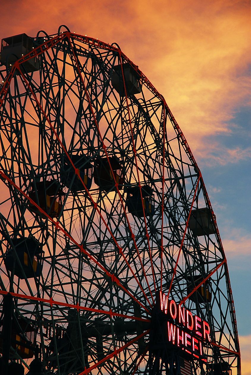 The giant Wonder Wheel Ferris wheel is silhouetted against a bright sunset sky on the boardwalk in Coney Island, New York. Editorial credit: James Kirkikis / Shutterstock.com