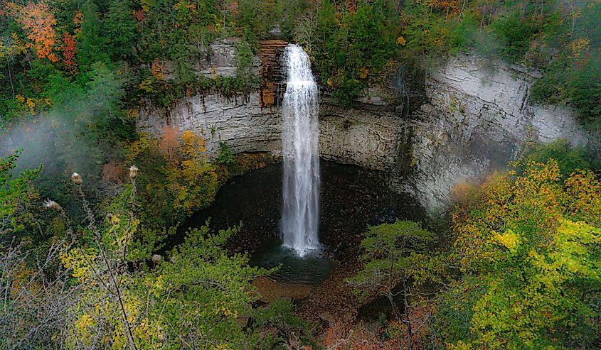 Photo of Falls Creek Falls in an autumn morning mist. Fall colors surround a ribbon of water falling from a rock cliff into a dark pool below. Taken at Falls Creek Falls State Park in Tennessee.