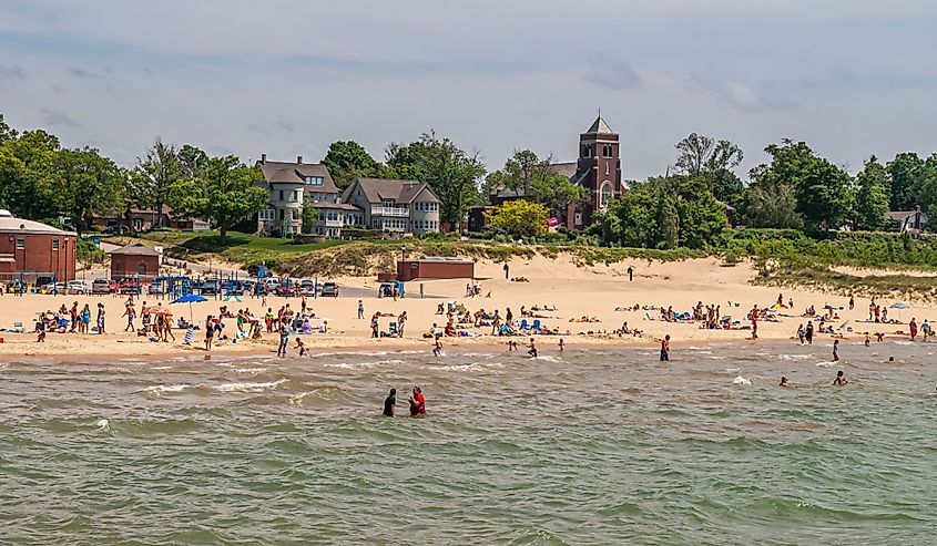 Dark brown stone Saint Basil Catholic church behind well occupied beige sand beach on Lake Michigan, South Haven.