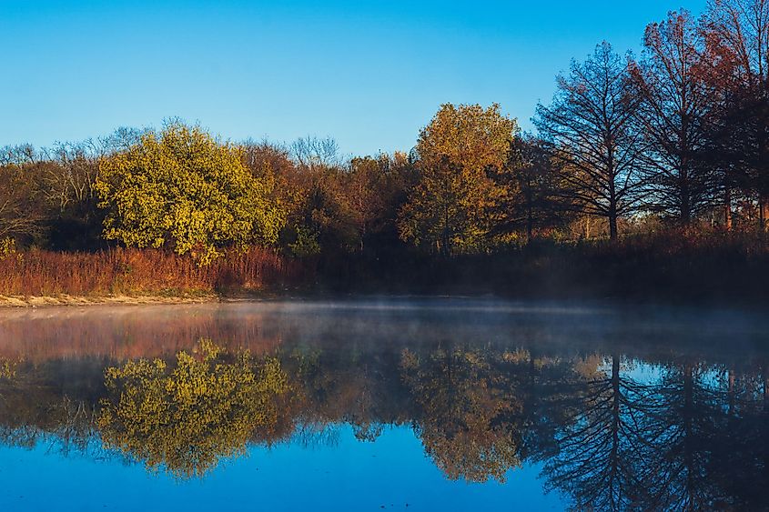 Vibrant trees reflected on the lake with early morning fog in Duck Creek Park, Garland, Texas