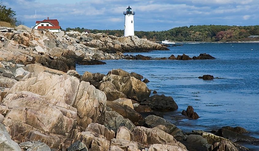 Portsmouth Harbor (Fort Constitution) lighthouse guides fishing boat during low tide along rocky coastline.