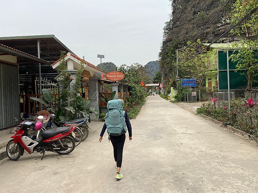 A female backpacker with a baby blue trekking bag walks a backroad in rural Vietnam.