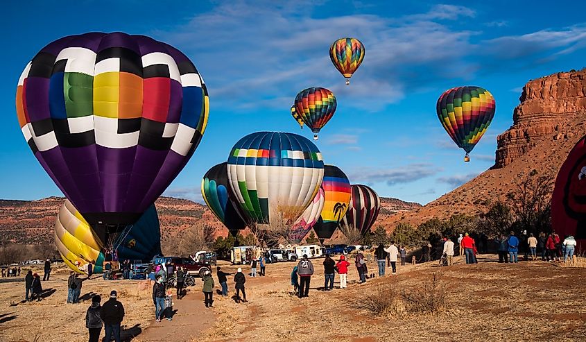 Spectators gather in open fields beneath beautiful red rock mesas to watch the hot air balloons in Kanab, Utah